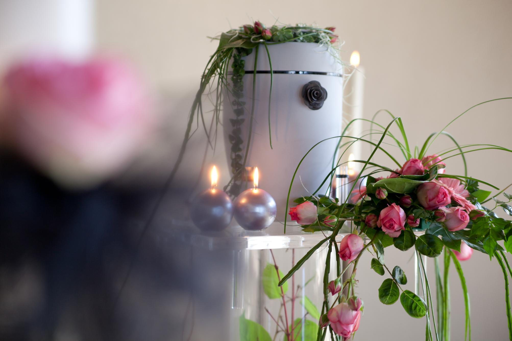 Blumenschmuck mit rosa Rosen und grünen Pflanzenarrangements auf einem Tisch, umgeben von Kerzen und einem weißen Behälter.